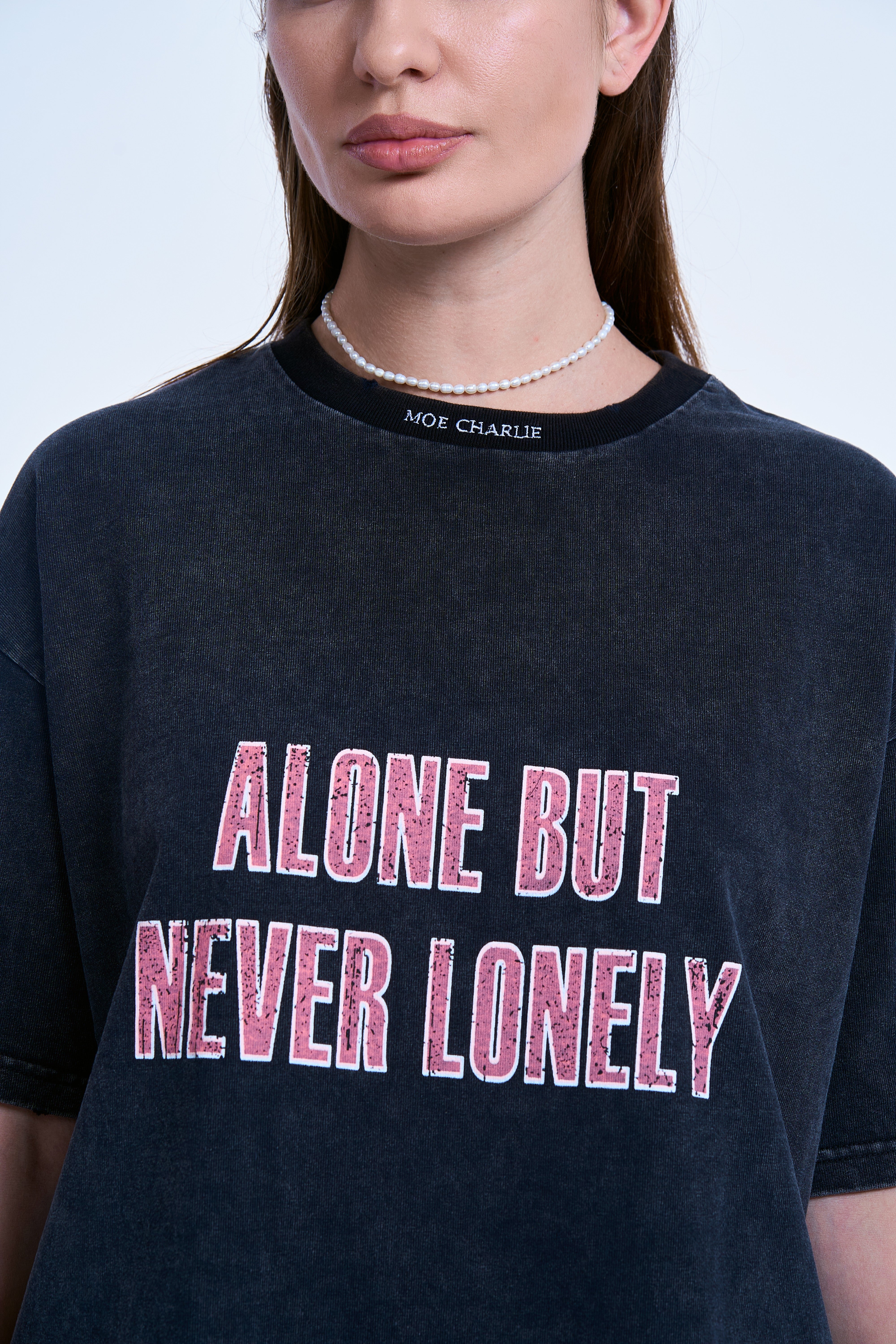 Nahaufnahme Print – pinke Block-Letter «Alone But Never Lonely» auf dunkelgrauem Acid-Wash-Stoff