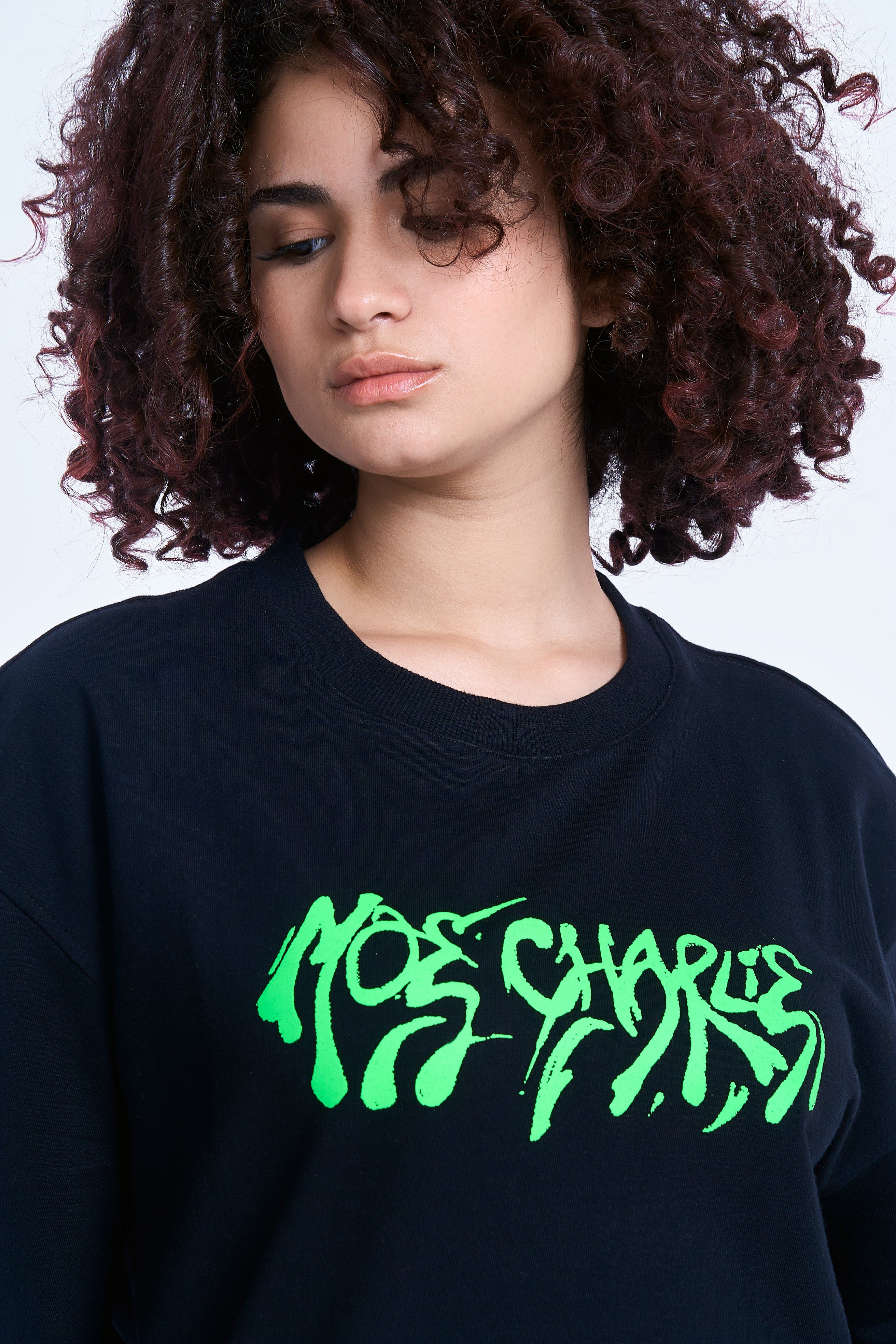 Detailansicht MOE CHARLIE Graffiti T-Shirt, neon-grüner Print im Vordergrund, weibliches Model, Blick gesenkt