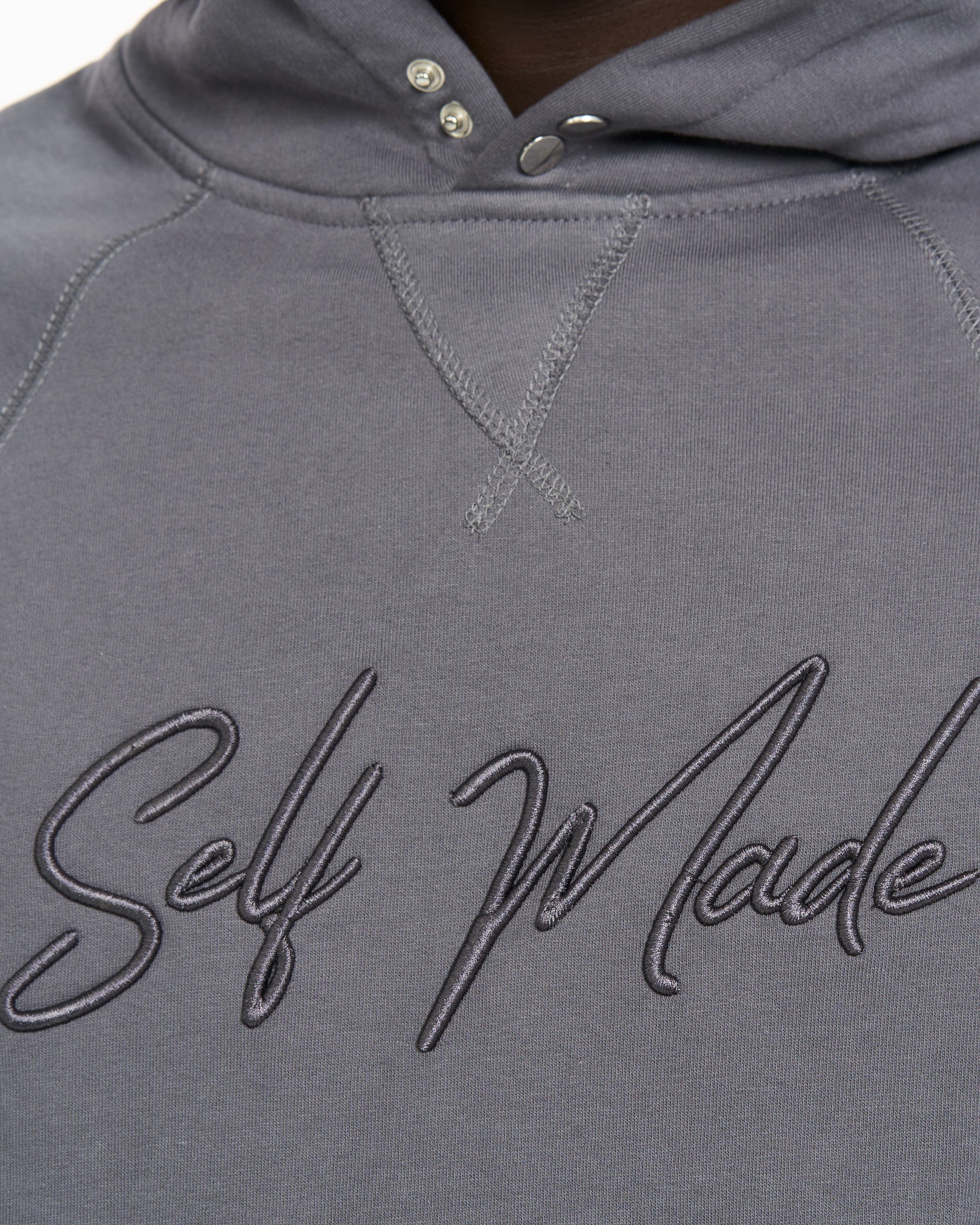 Detailaufnahme Self-Made-Stickerei auf grauem Hoodie MOE CHARLIE, Druckknopf an der Kapuze sichtbar