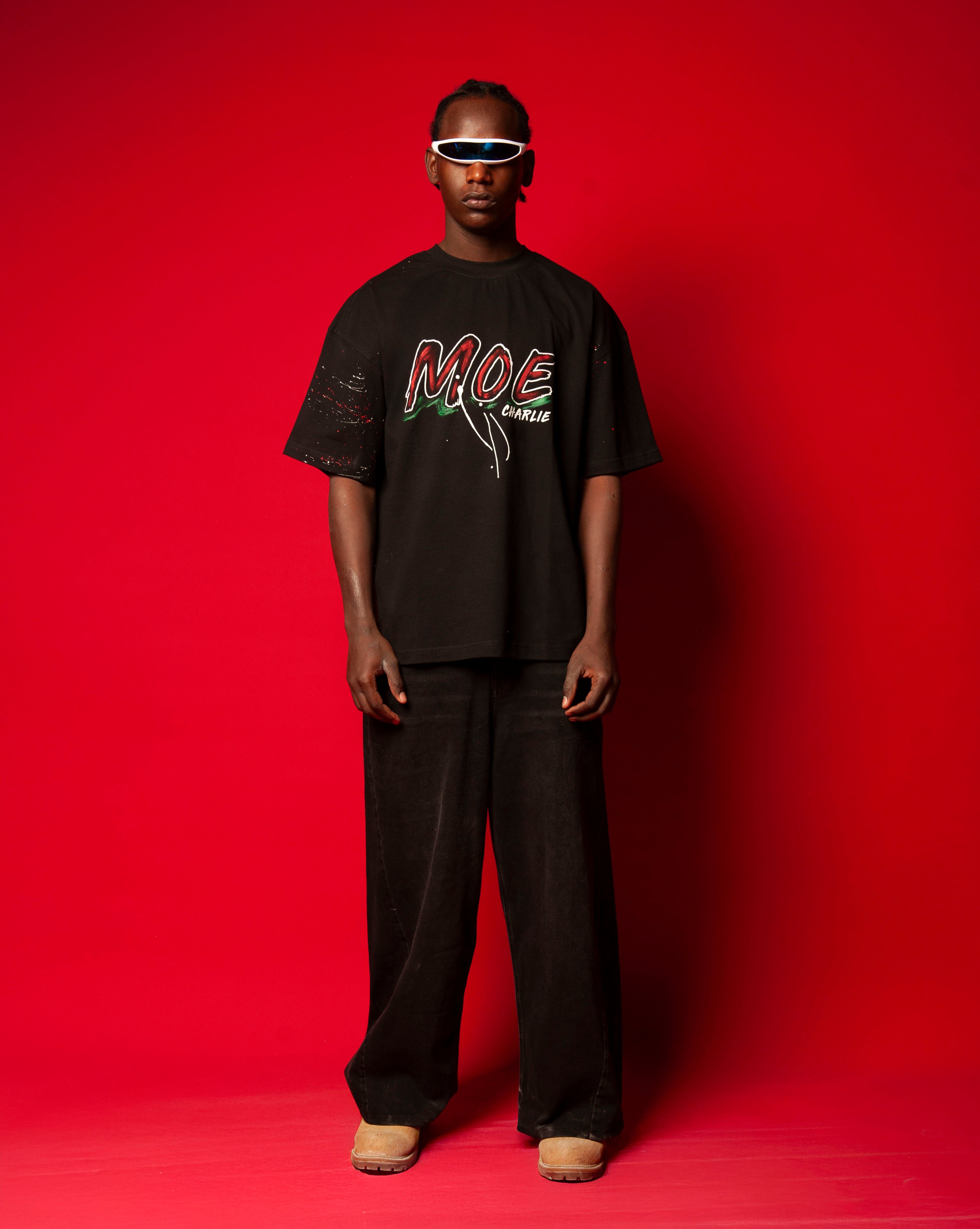 MOE CHARLIE Moe T-Shirt Schwarz, Frontansicht Ganzkoerper, schwarzes Tee mit rotem Graffiti-MOE-Print, weisser Visor