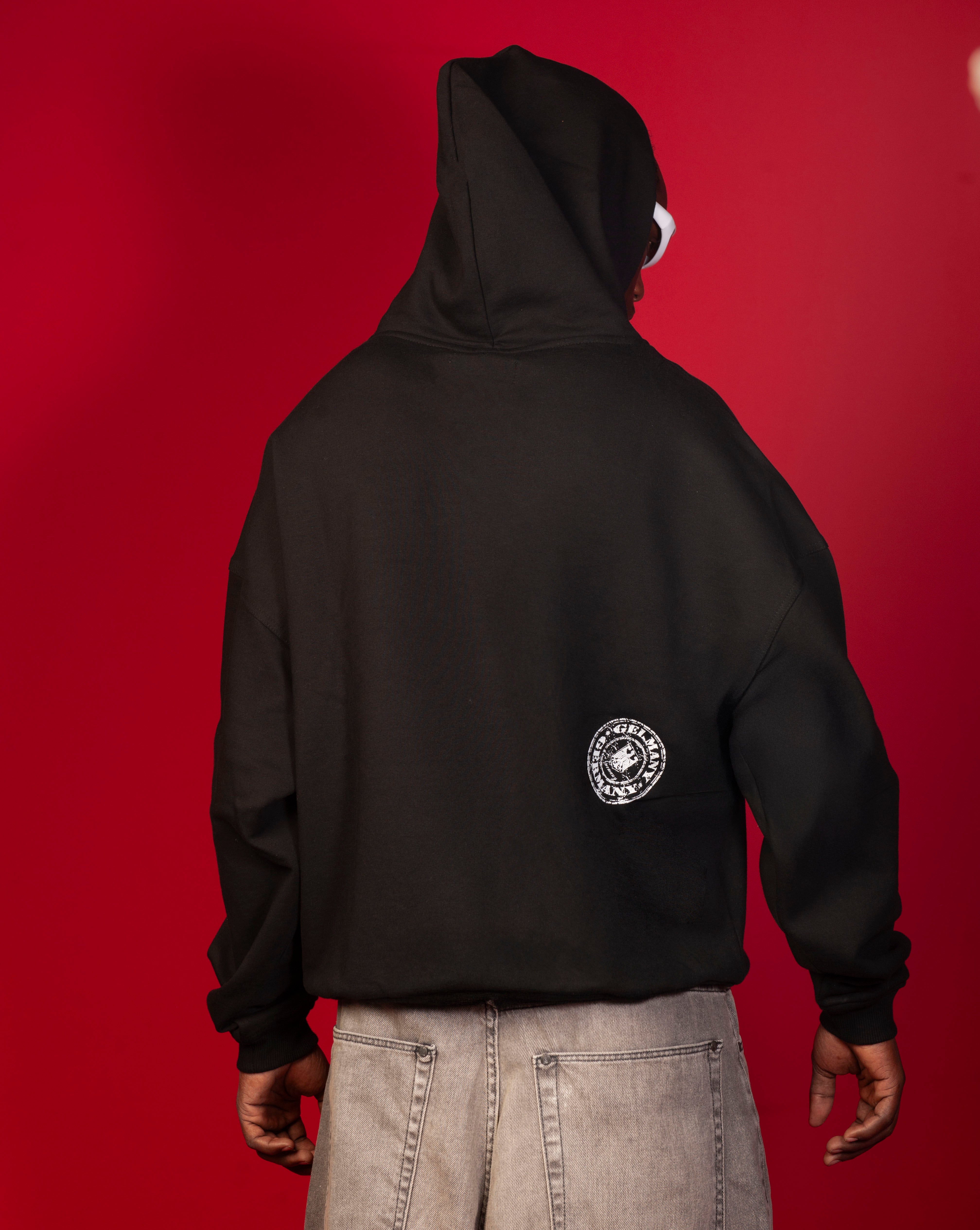 Rueckenansicht Stampel Hoodie MOE CHARLIE, schwarzer Ruecken mit weissem Siegel-Logo, Kapuze und Jeans