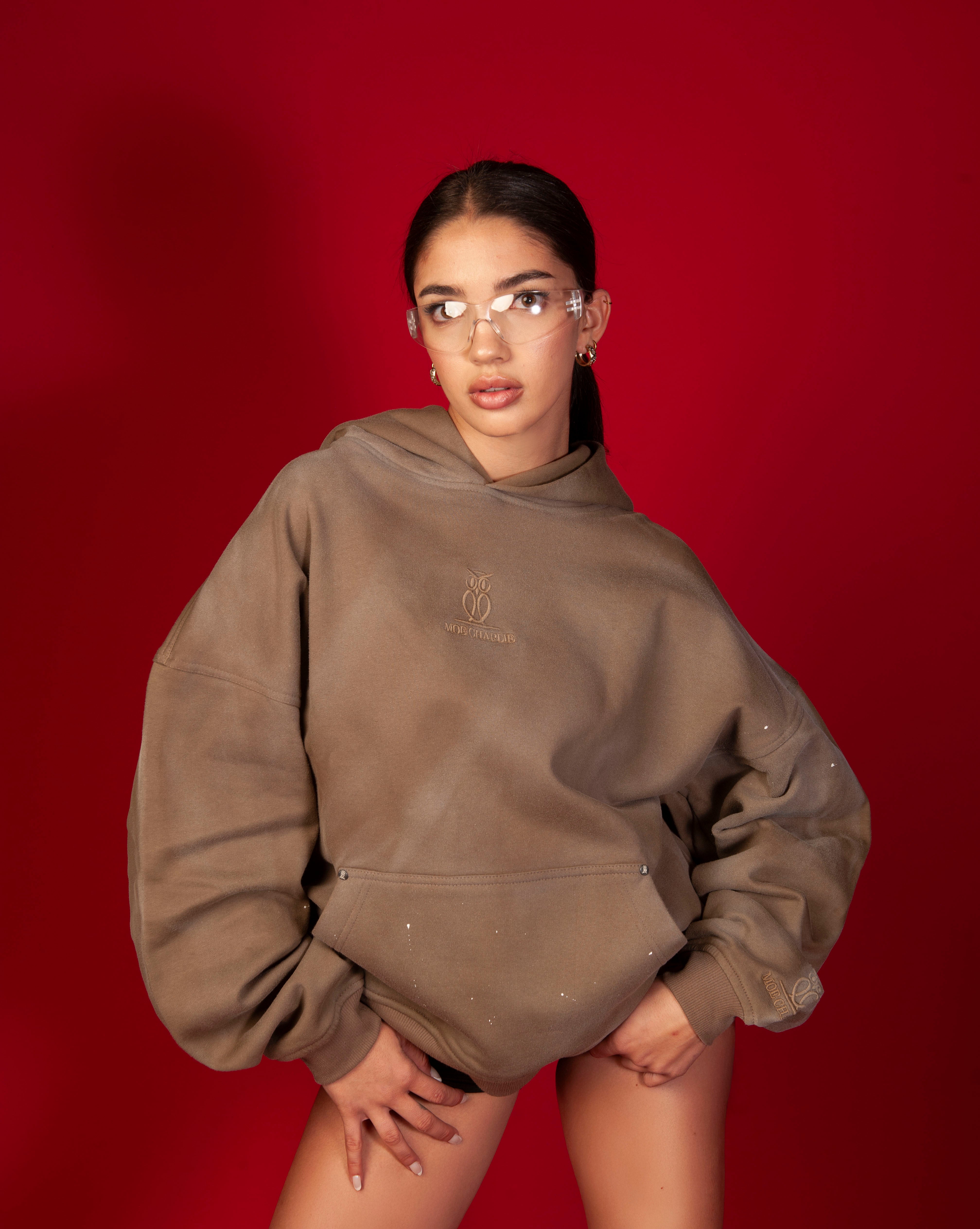 Artist Hoodie MOE CHARLIE, weiblich vorgebeugt, taupe Hoodie mit tonal gesticktem Owl-Logo und schwarzen Shorts