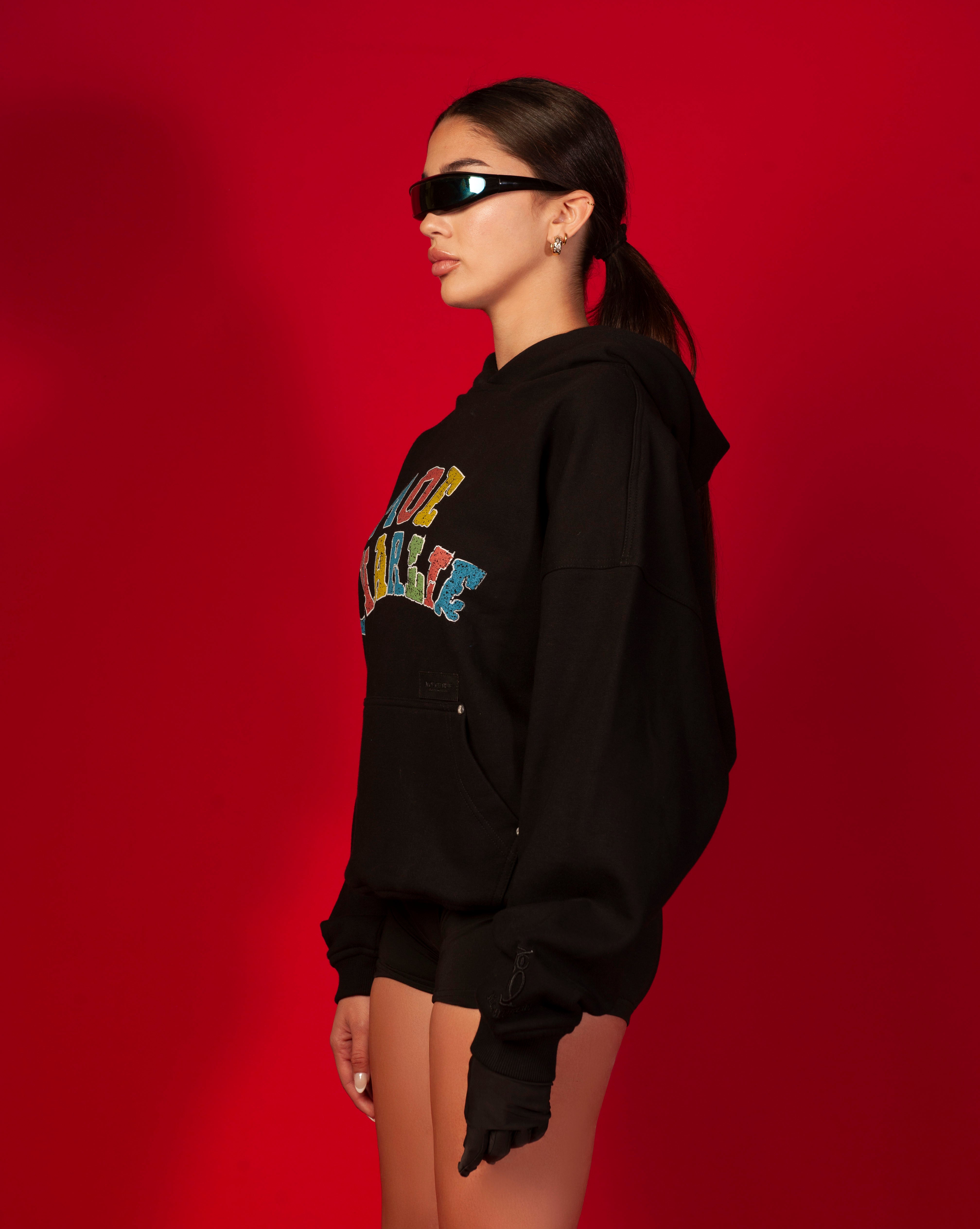 Seitenansicht Google Hoodie MOE CHARLIE weiblich, Visor-Brille, schwarze Handschuhe und Mini-Shorts