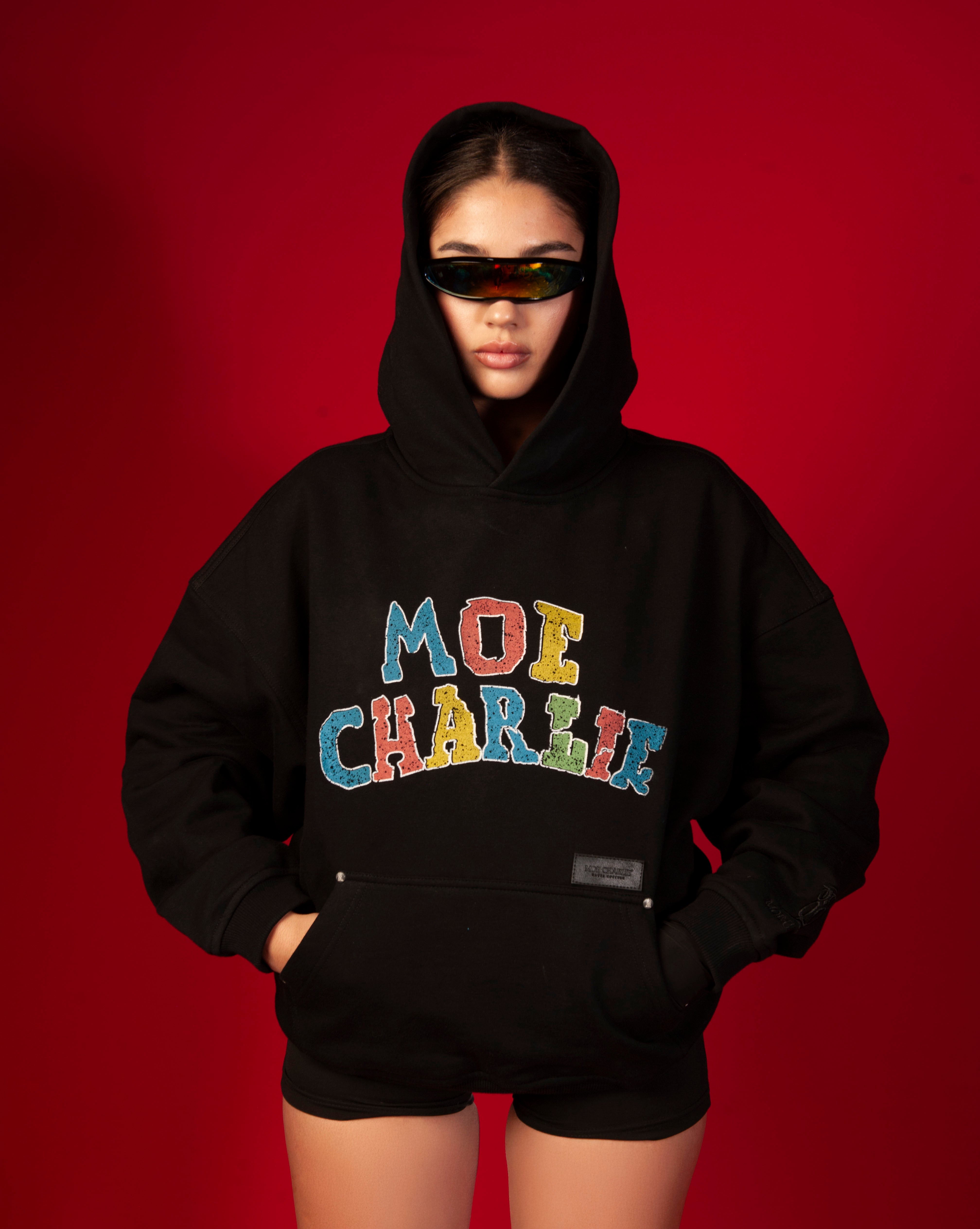 Google Hoodie MOE CHARLIE weiblich, Kapuze auf, bunter MOE-CHARLIE-Print, Regenbogen-Visor und Shorts