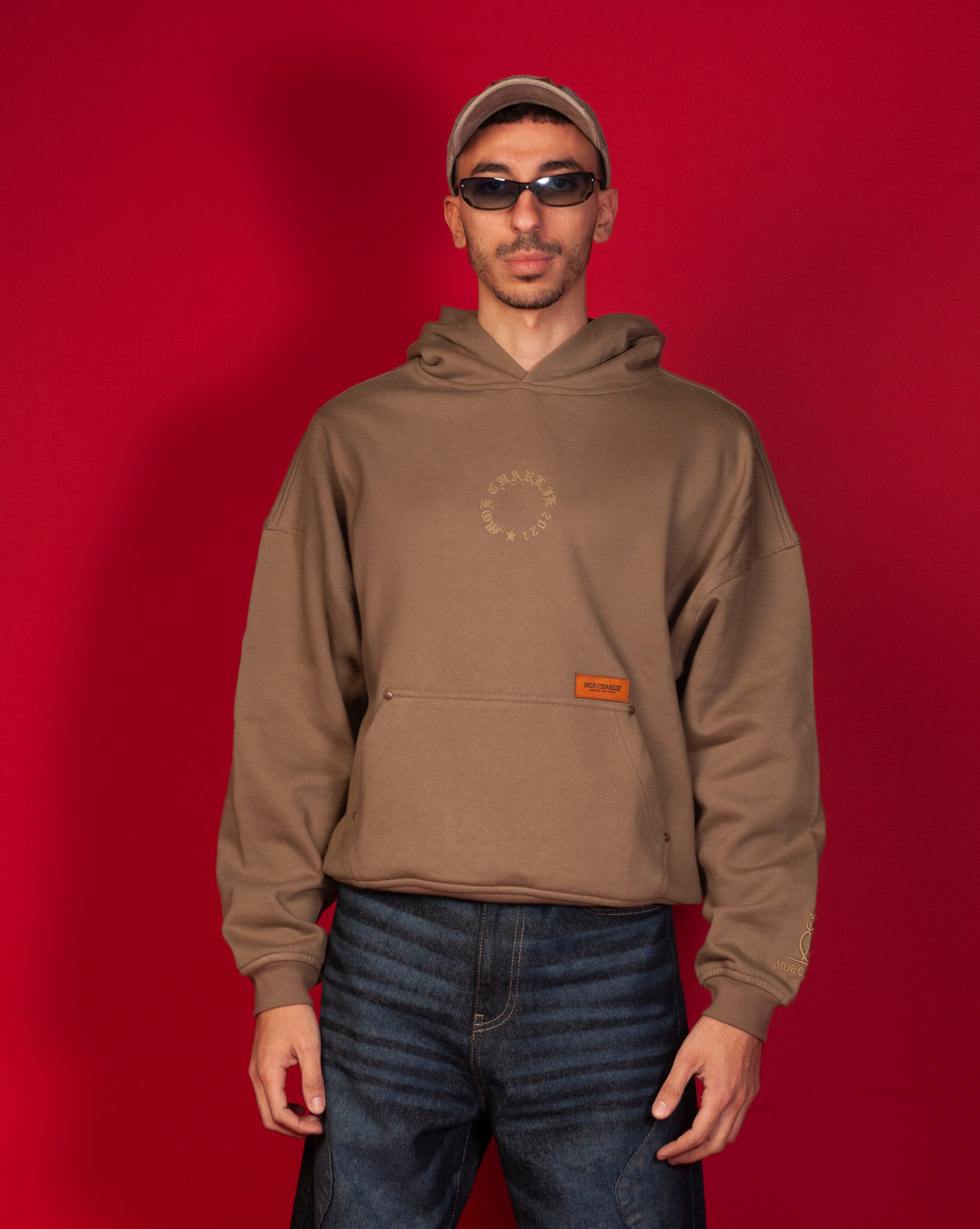 Moe Charlie Hoodie MOE CHARLIE, Frontansicht maennlich, caramel-brauner Hoodie mit Leder-Patch, Olive-Cap