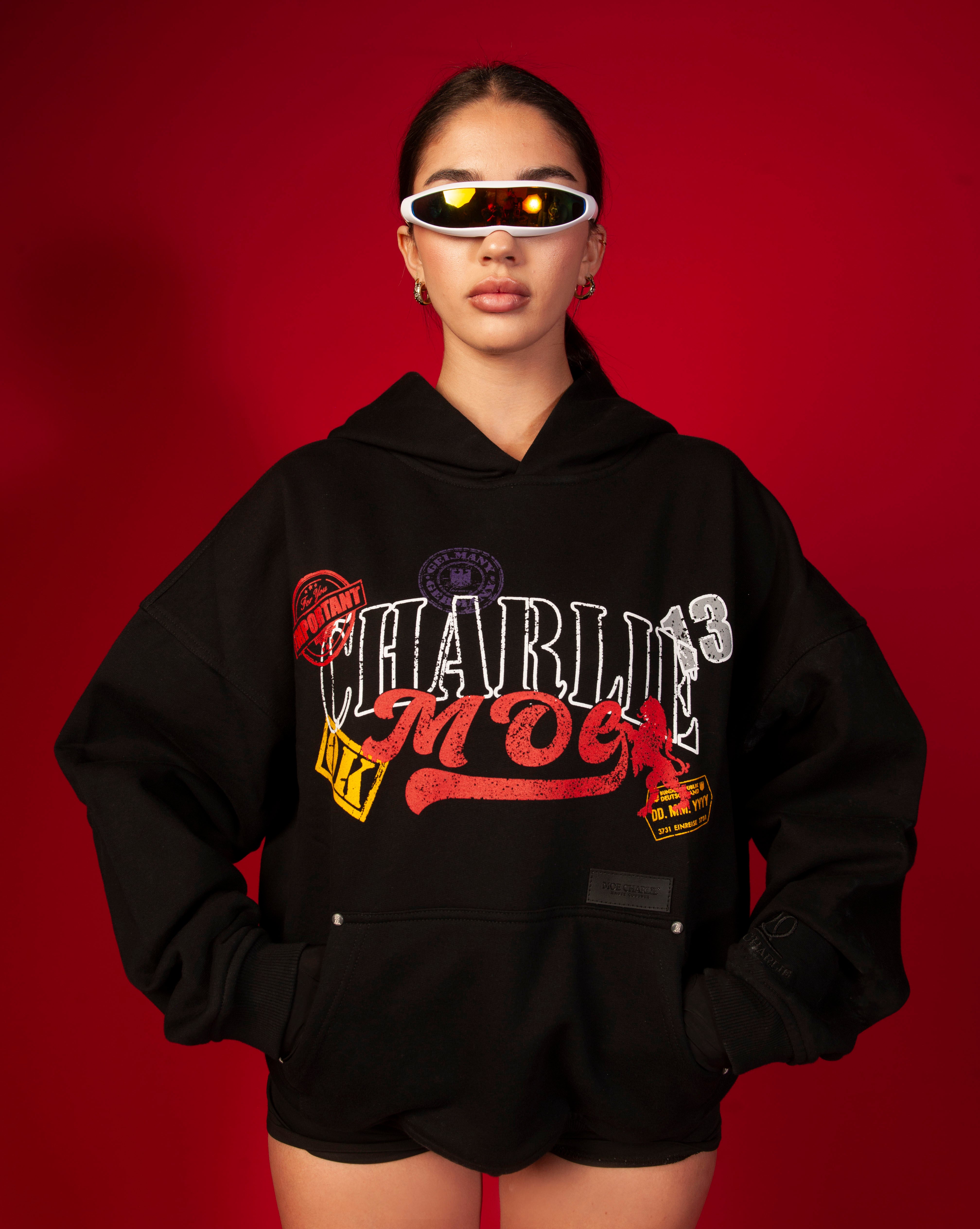 MOE CHARLIE Stampel Hoodie, weiblich mit Haenden in Hueften, schwarze Handschuhe und schwarze Shorts