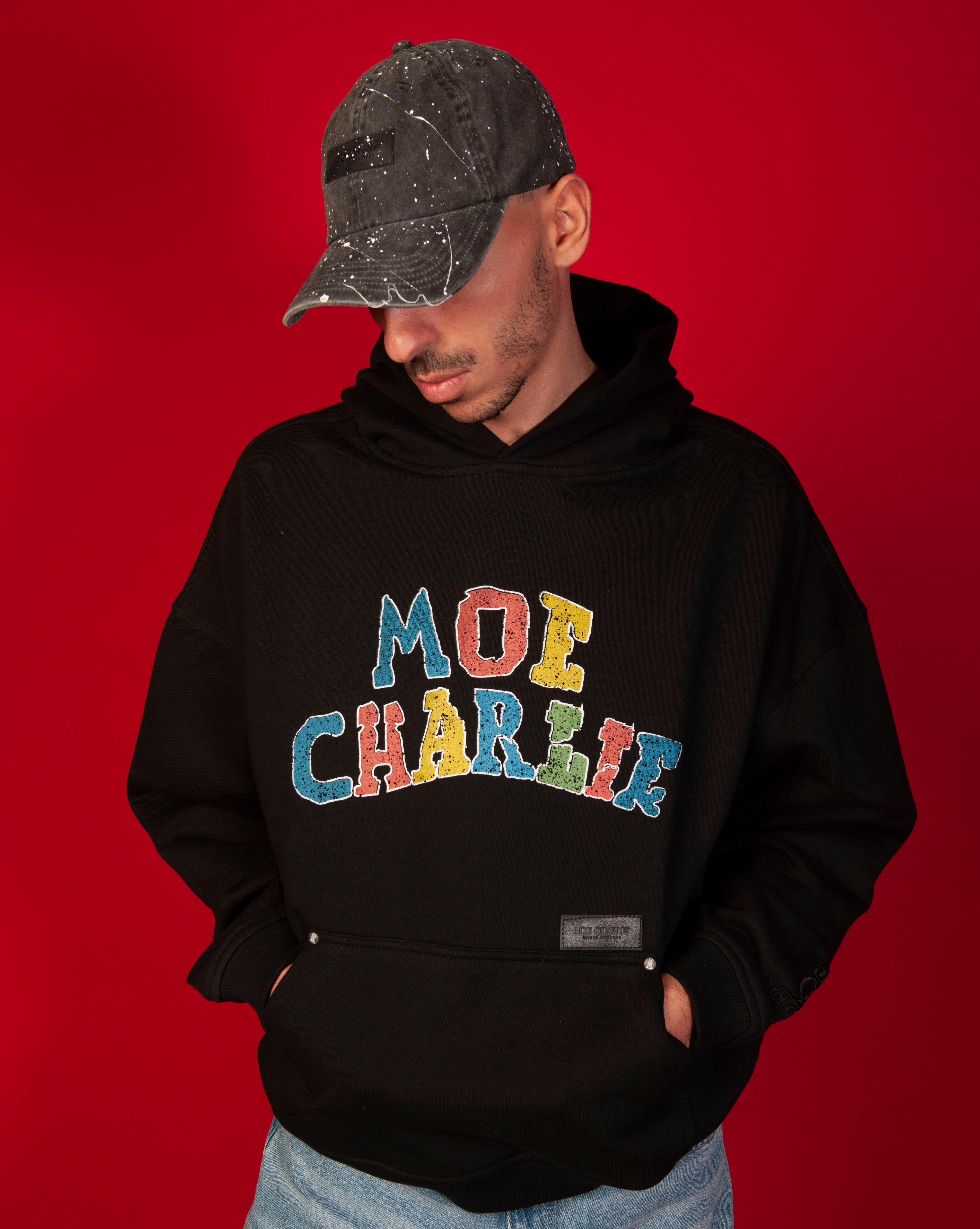 MOE CHARLIE Google Hoodie, Brustansicht maennlich, bunter MOE-CHARLIE-Print im Detail, Haende in Tasche