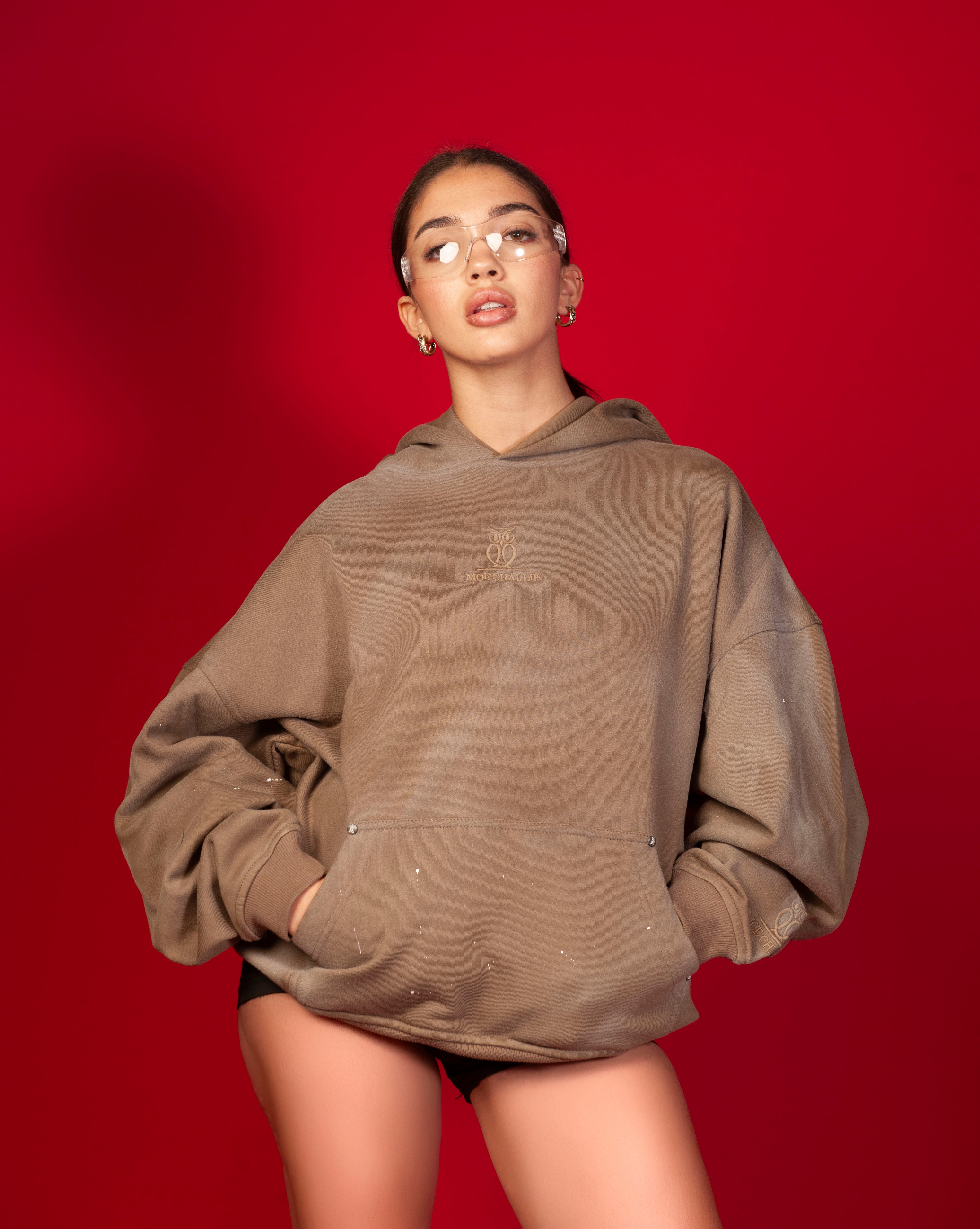 Artist Hoodie MOE CHARLIE, Frontansicht weiblich, taupe Oversize-Hoodie mit tonal gesticktem Logo, transparente Brille