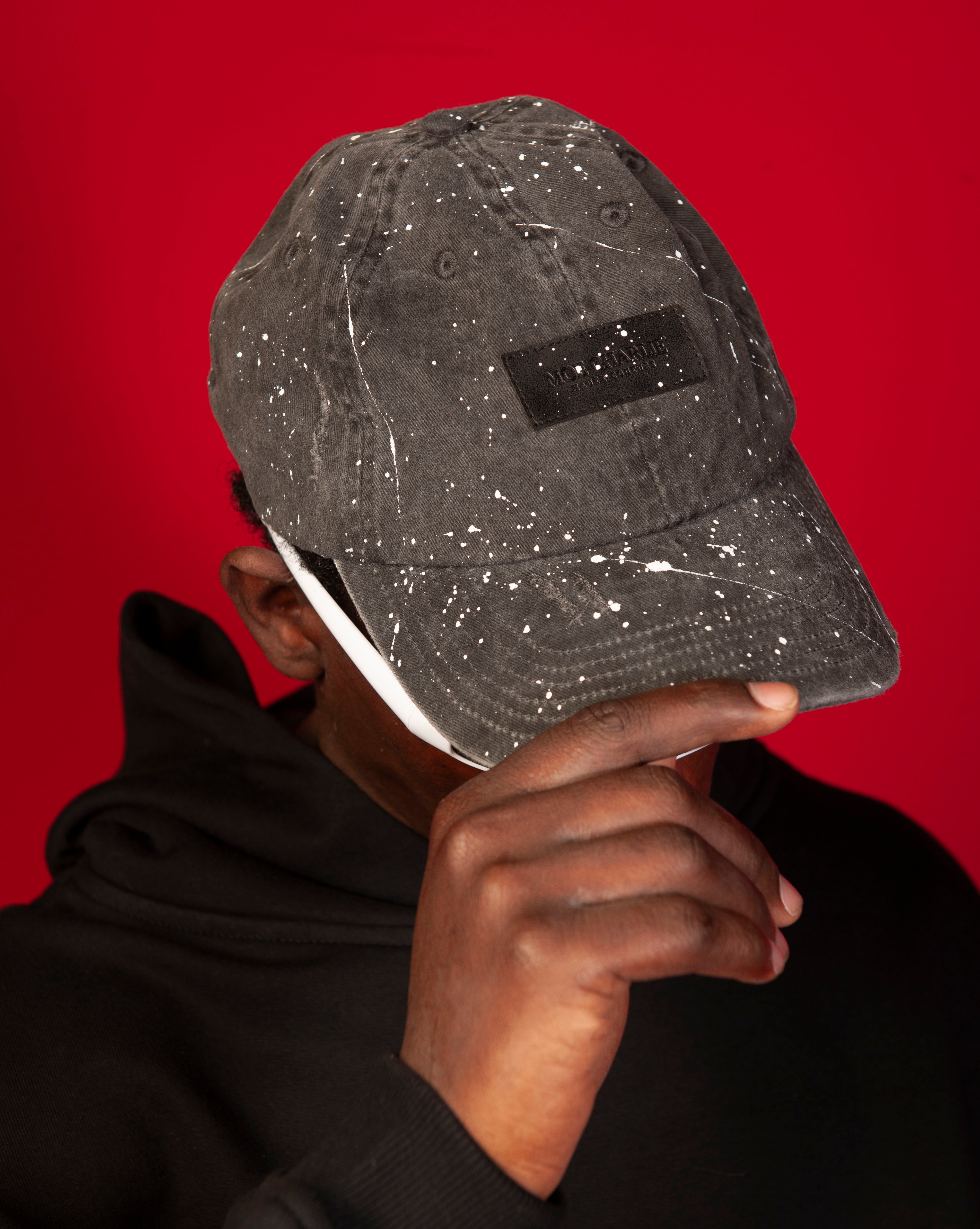 Destroyed MOE CHARLIE Cap, zweiter Traeger haelt Cap nach oben, schwarzes Farbspritzer-Cap, schwarze Label-Patch