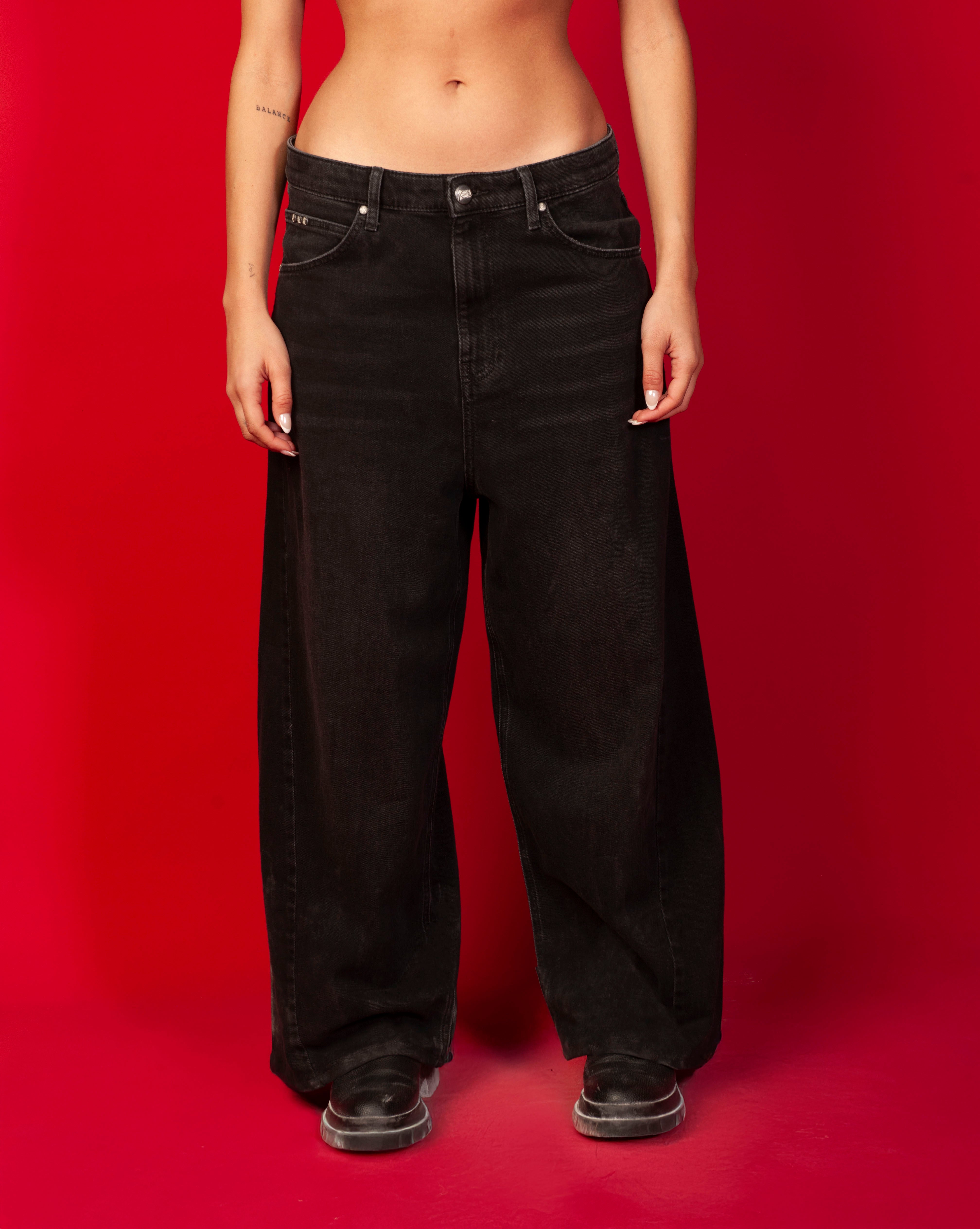 Extra Baggy Denim Schwarz MOE CHARLIE, Frontansicht weiblich ab Taille, breite Hosenbeine auf rotem Hintergrund