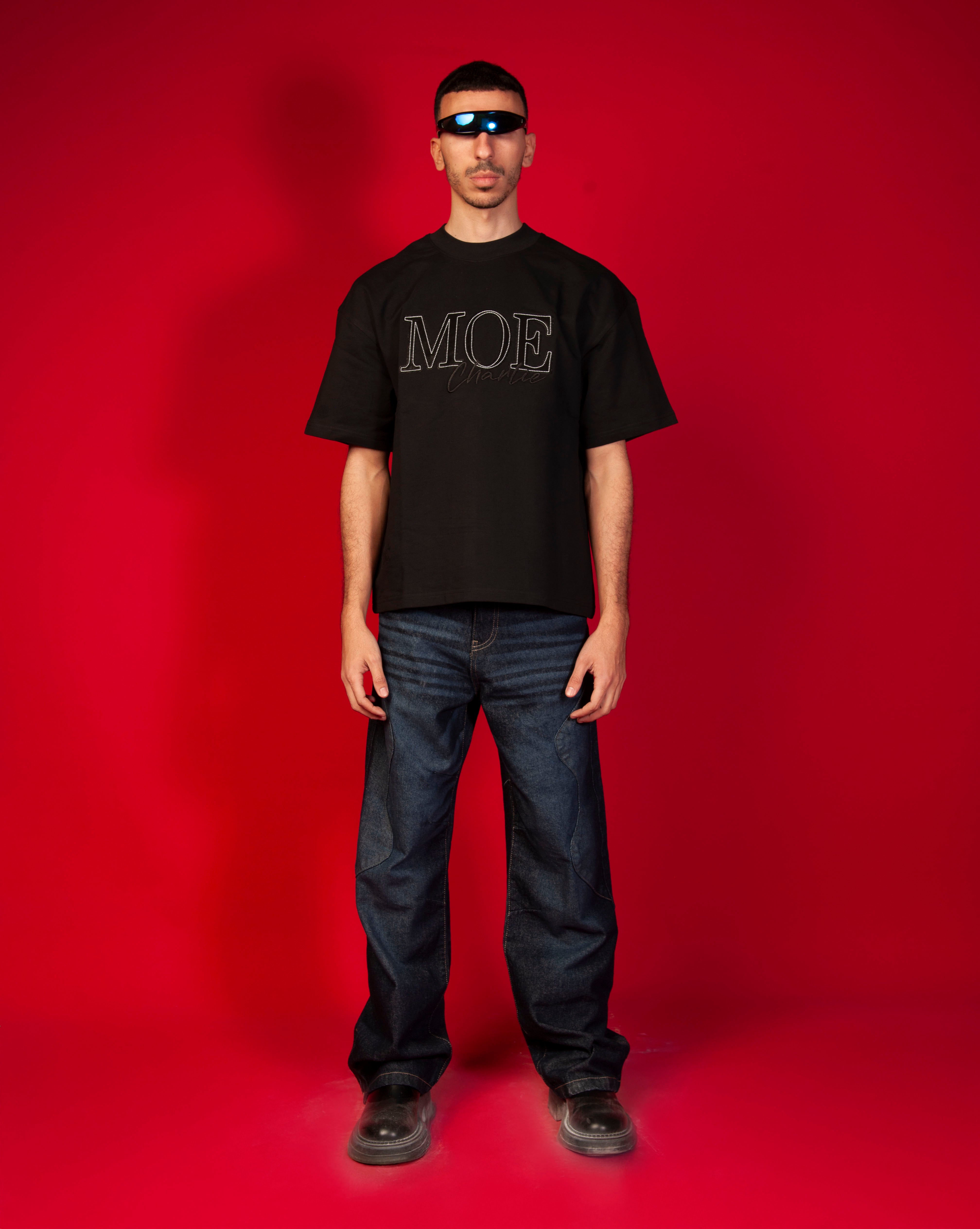 MOE Oversize T-Shirt MOE CHARLIE, Frontansicht maennlich Ganzkoerper, schwarzes Tee, MOE-Charlie-Schrift, dunkle Jeans
