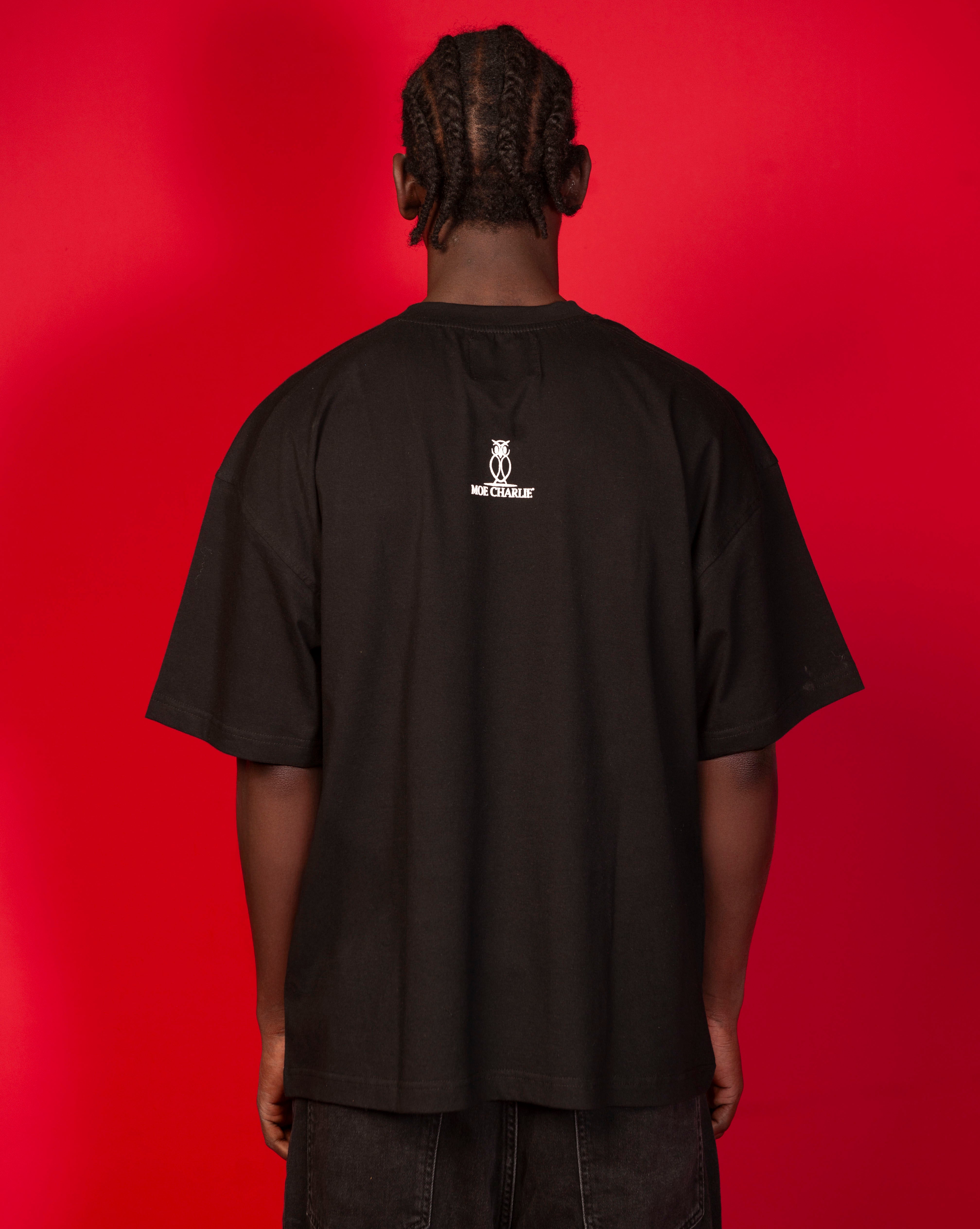 Nahaufnahme Ruecken Moe T-Shirt Schwarz MOE CHARLIE, weisses Owl-Logo mittig auf schwarzem Tee, schwarze Hose