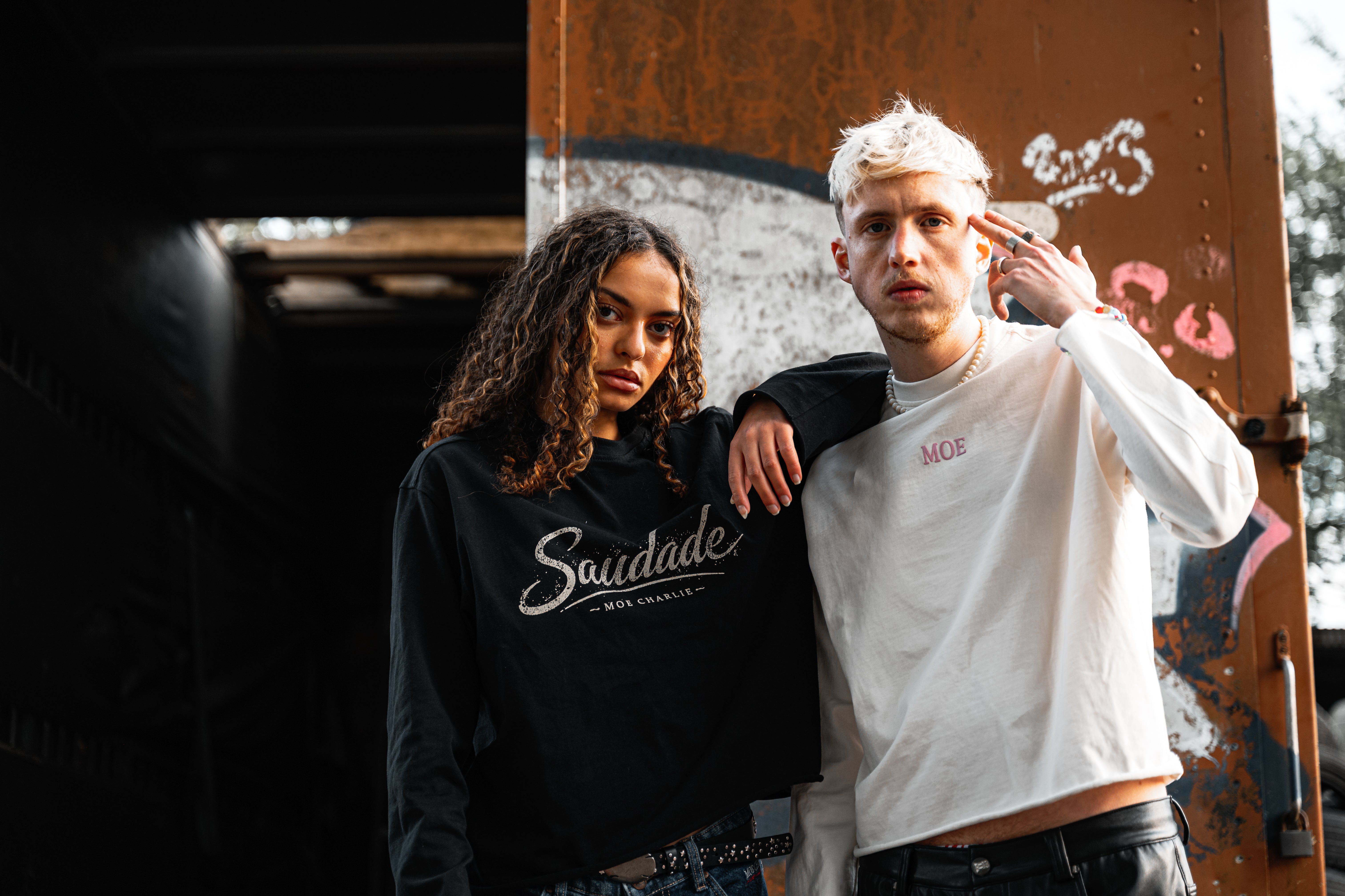 Frau mit schwarzem Saudade Longsleeve, rechts daneben Mann mit creme cropped MOE longsleeve